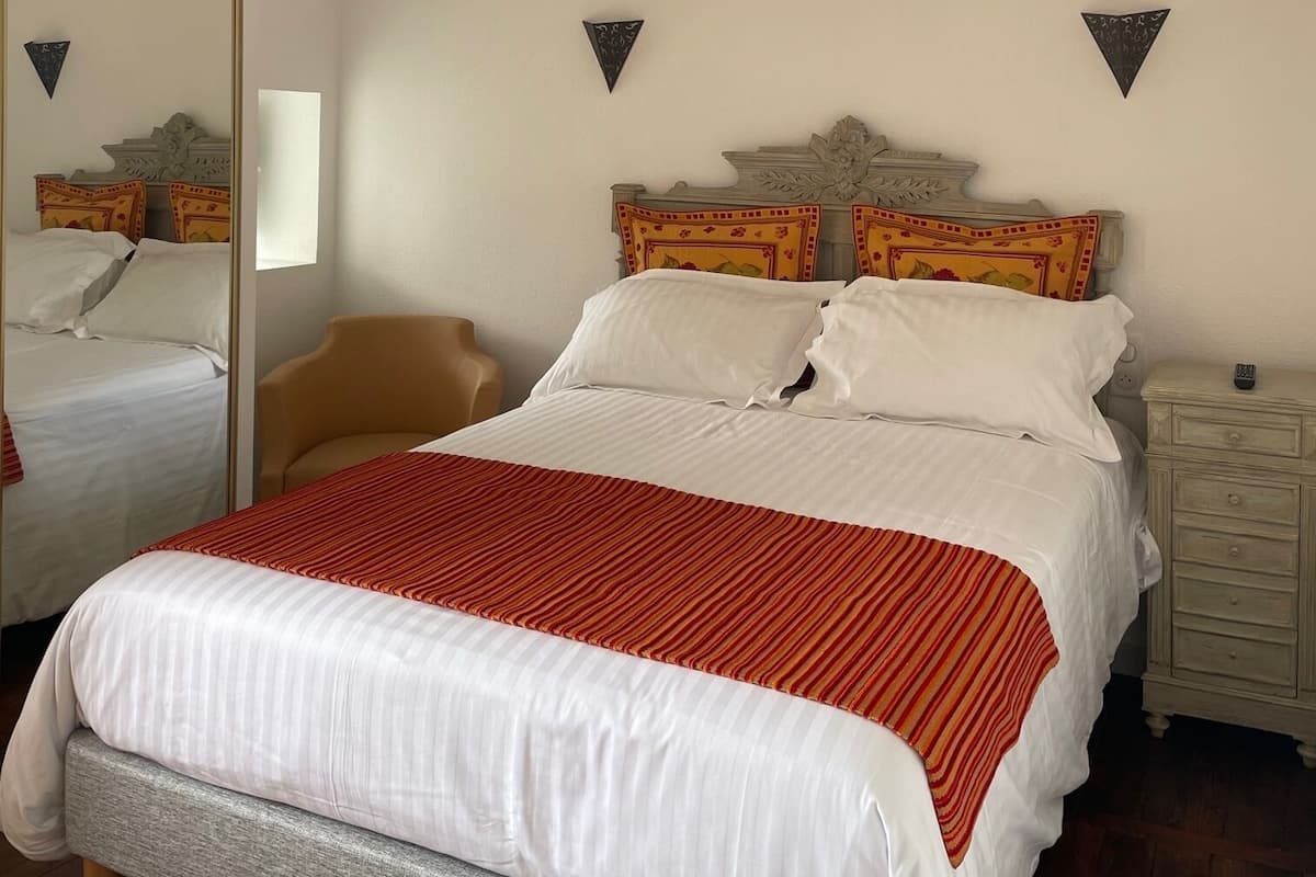 Une chambre bien rangée, avec un grand lit, une chaise, une table de chevet et un miroir.