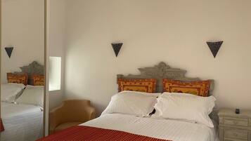 A neatly arranged bedroom with a large bed, a chair, a nightstand, and a mirror.