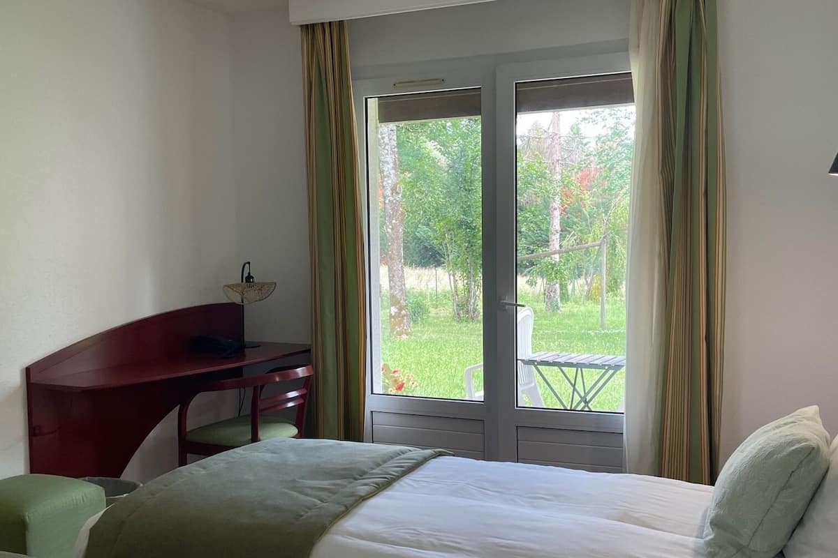 Une chambre d’hôtel avec deux lits, un bureau et une vue sur un jardin, accessible par une porte vitrée.