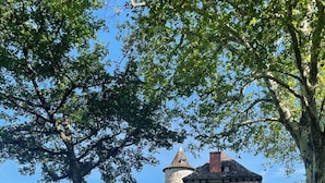 Ein Gebäude aus Stein mit einem Turm, umgeben von Bäumen und einer Rasenfläche.
