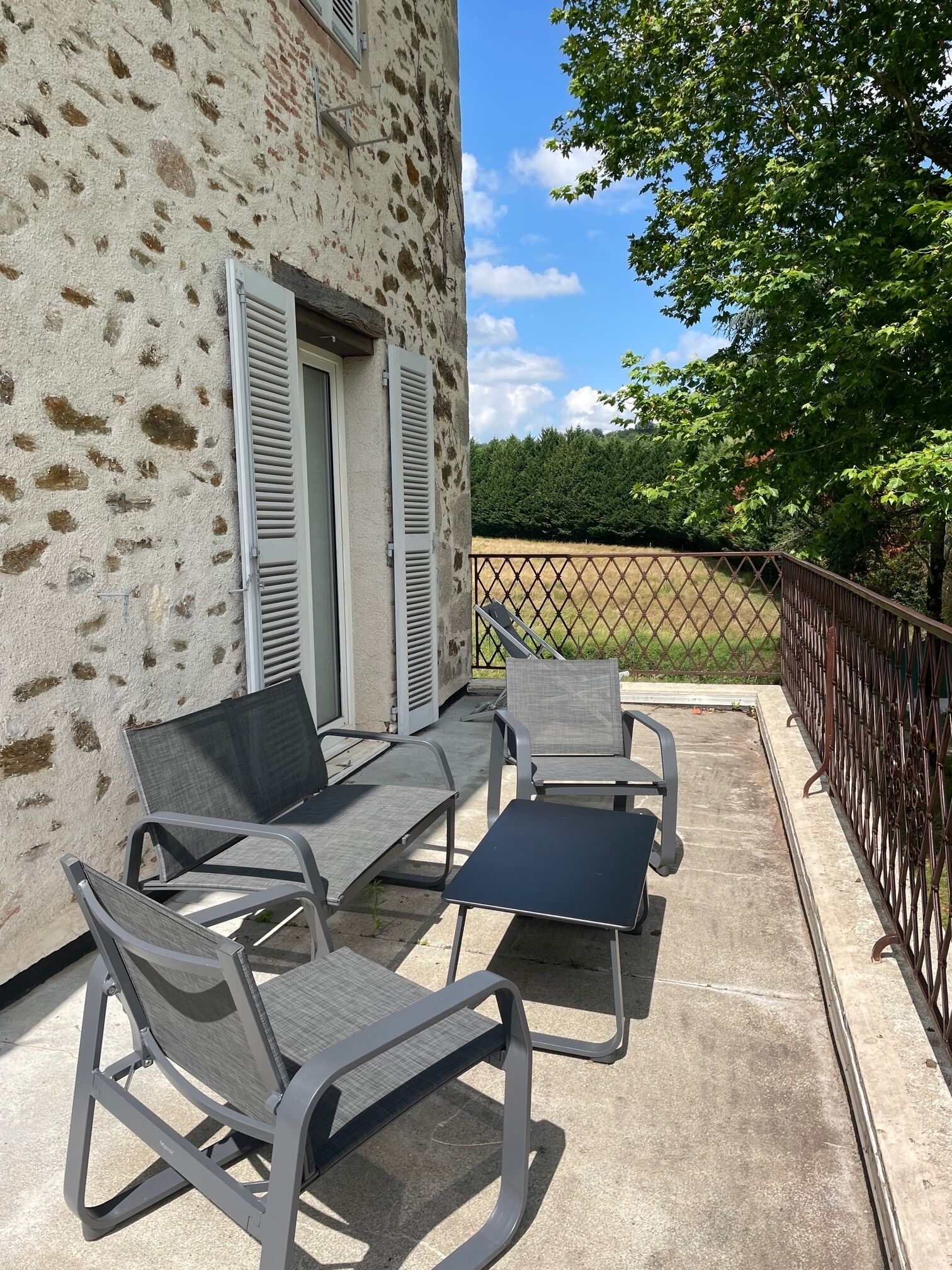 An outdoor patio with two grey metal chairs and a small table, a stone wall, and a metal fence.
