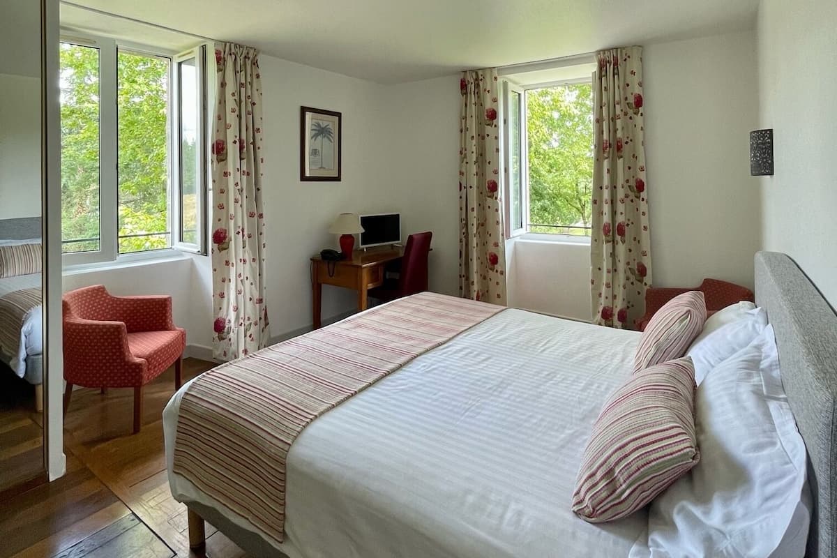 Une chambre à coucher avec un lit, un bureau, une chaise et de grandes fenêtres.