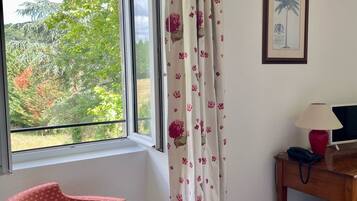 A room with a window, a chair, a desk with a lamp, and a framed picture on the wall.