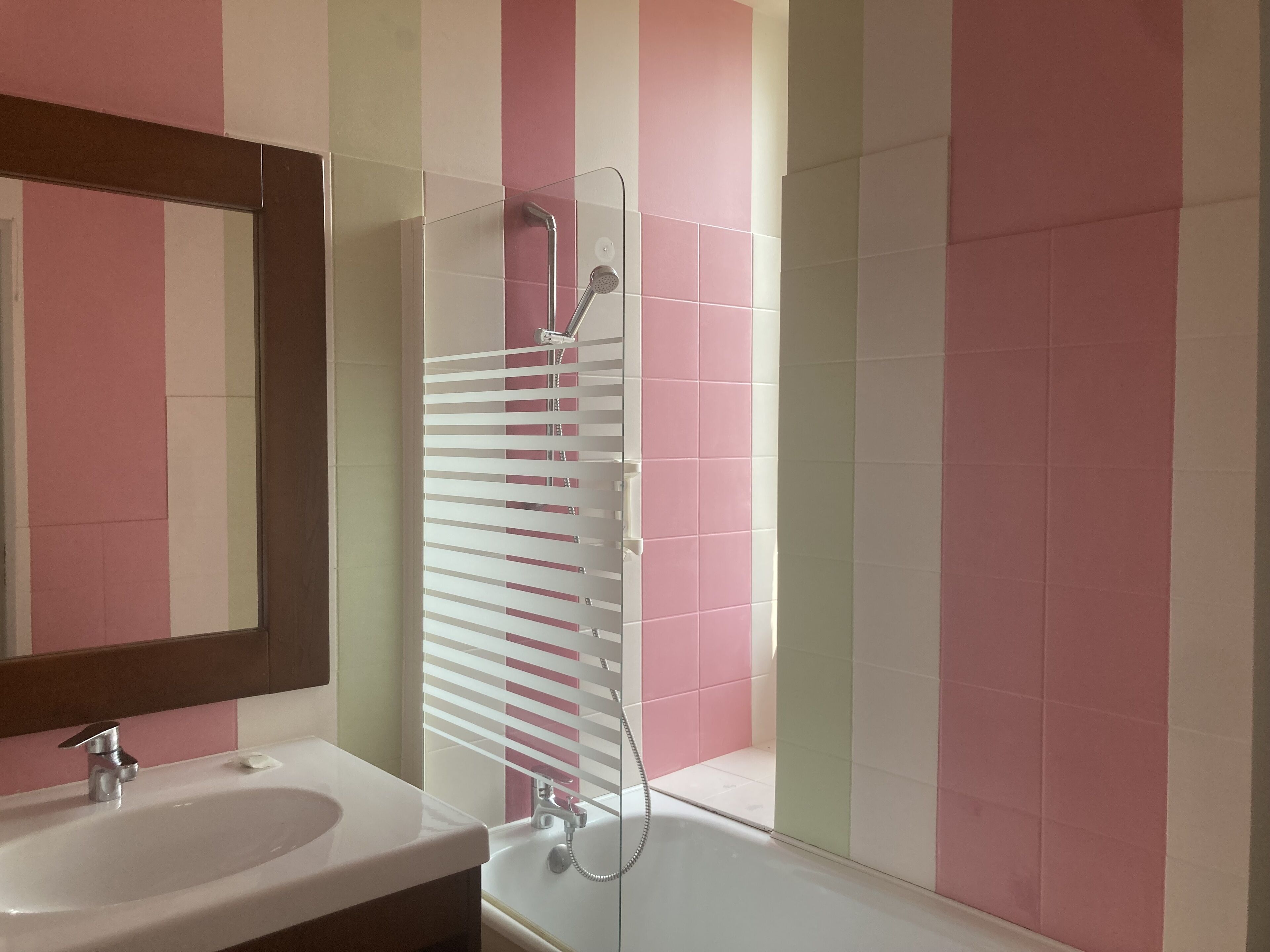 A bathroom with a sink, mirror, shower, and striped walls.