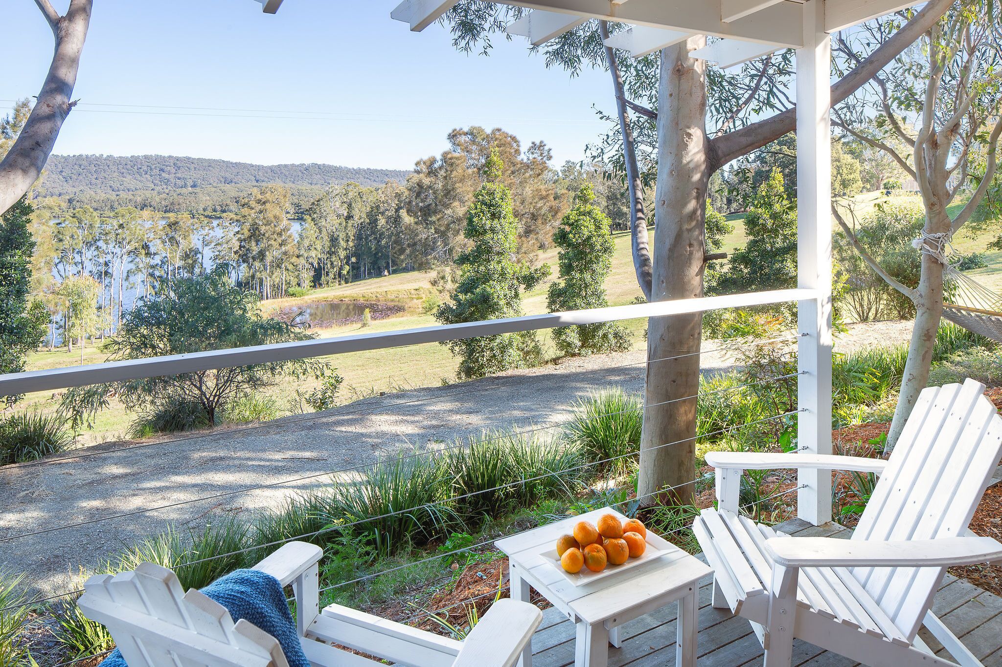 A covered outdoor seating area with white Adirondack chairs and a table with oranges.