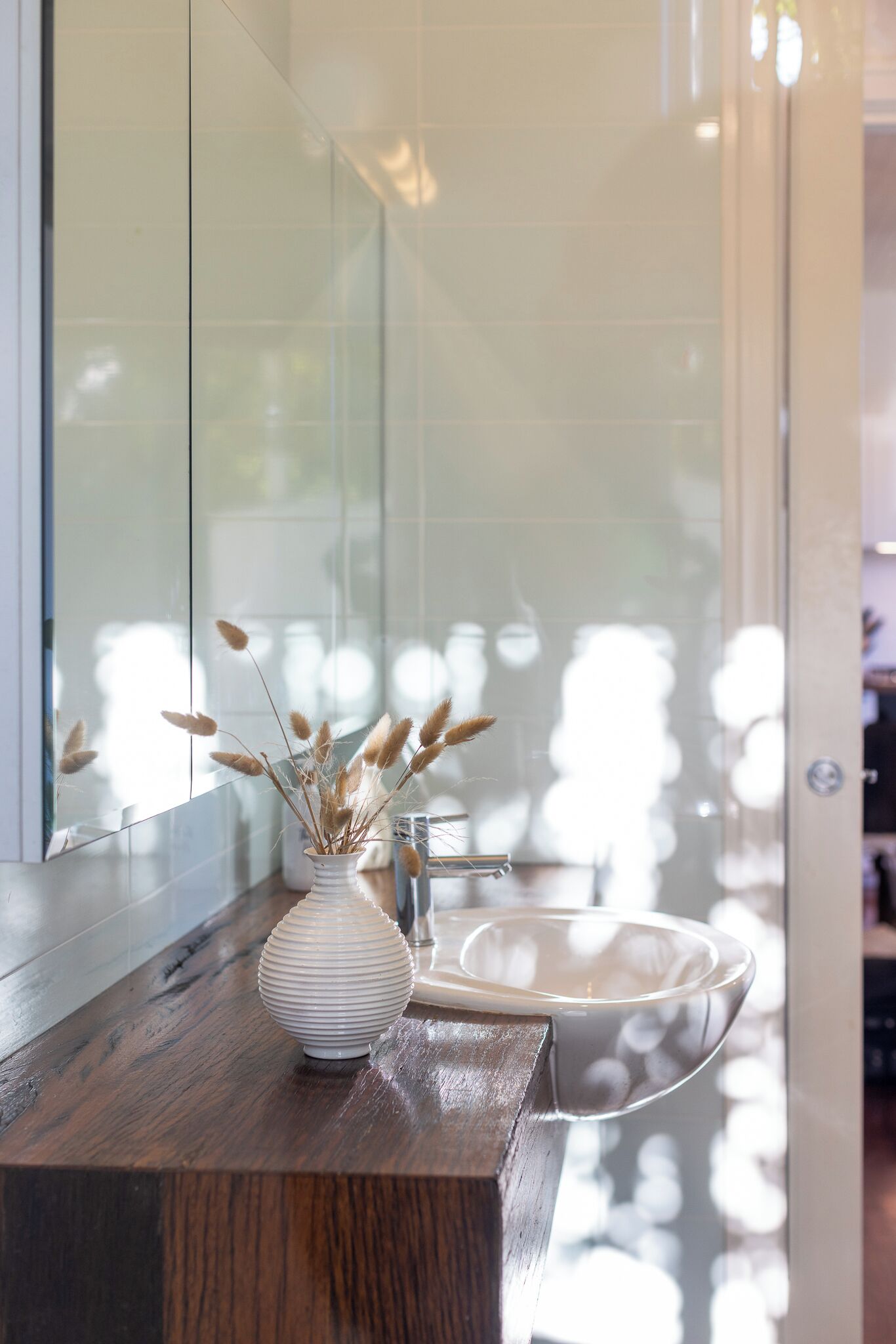 Een badkamer met een houten aanrecht, een witte vaas met gedroogd pampasgras en een witte wastafel.