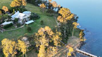 An aerial view of a coastal property with a large house, a dock, and a bridge leading to a pier.