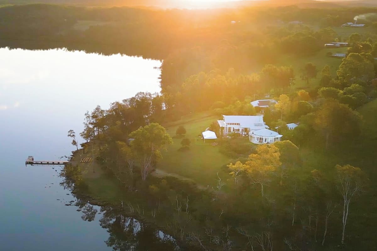 A lakeside property with a dock extending into the water, surrounded by trees and a few buildings.