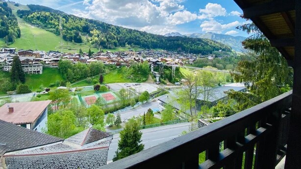 Une vue depuis un balcon donnant sur une ville avec ses bâtiments, ses rues et ses collines verdoyantes.
