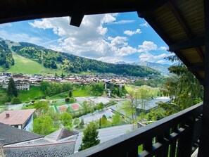Vista de uma varanda com vista para uma cidade, com edifícios, estradas e colinas verdes.