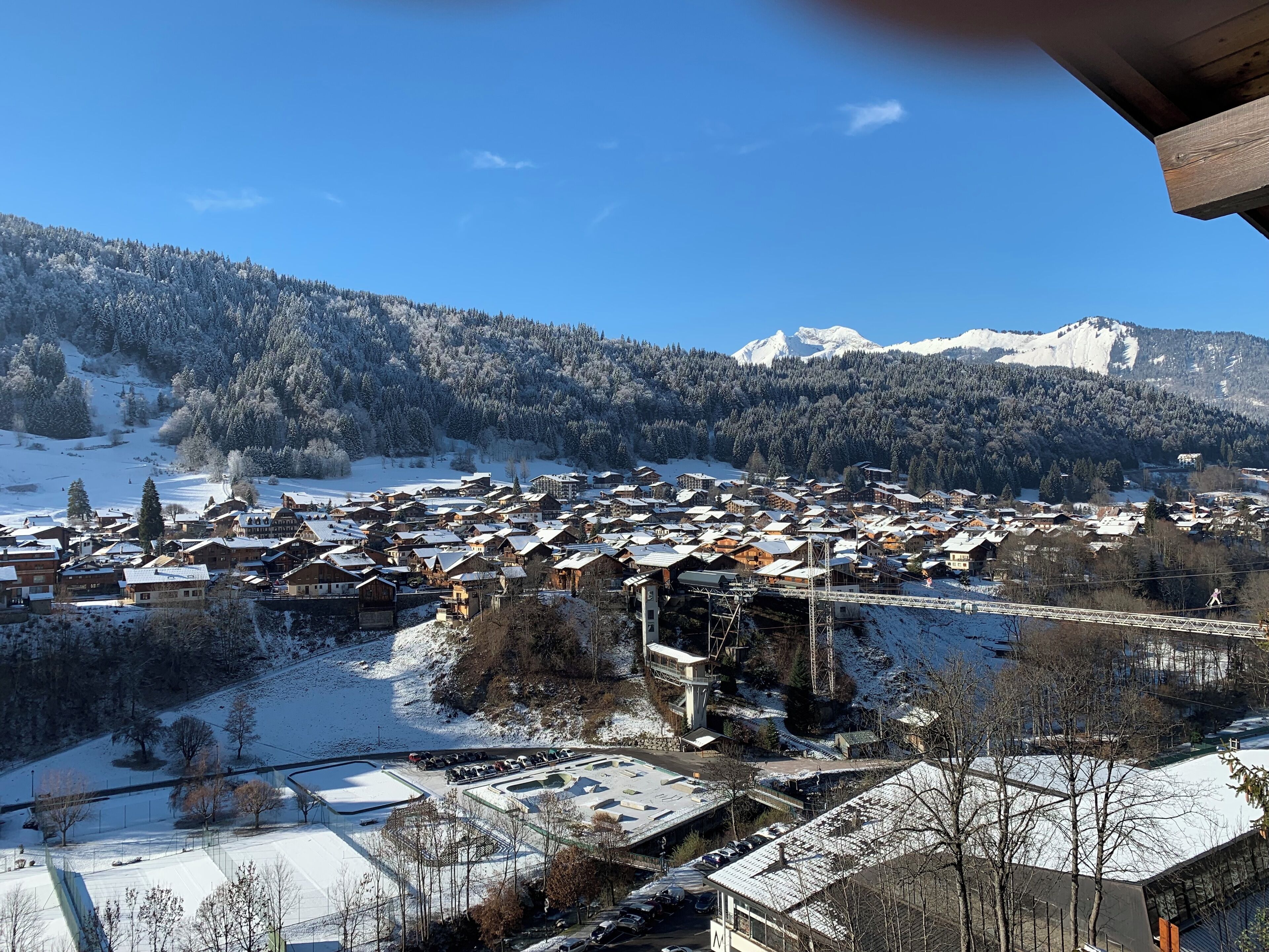 En snötäckt by med traditionella trähus, en skidlift och ett berg i bakgrunden.