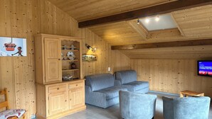 Une pièce chaleureuse, avec des murs en bois, un canapé, deux fauteuils, une armoire et un téléviseur.