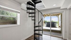 Un intérieur moderne avec un escalier en colimaçon, de grandes fenêtres et une vue sur une terrasse extérieure.
