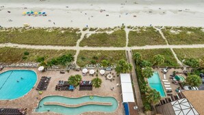 Vue aérienne d’un complexe hôtelier doté de deux piscines, d’une plage et d’un espace détente avec des parasols.