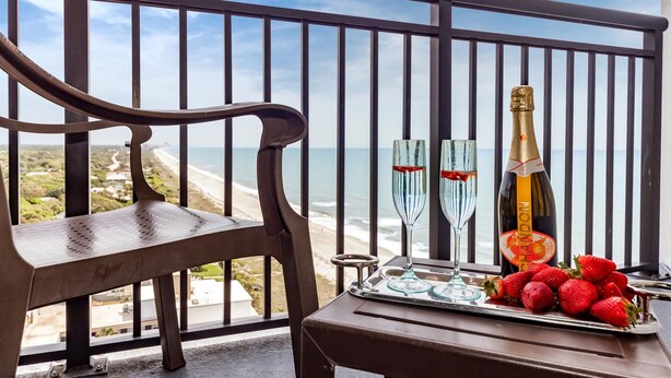 Un balcon avec une chaise en bois, deux coupes à champagne, une bouteille de champagne et une assiette de fraises.