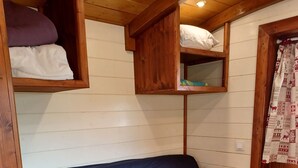 A wooden cabin interior with a blue sofa, yellow pillows, and wooden shelves above. - Roulottes a la Ferme sur le Plateau du Vercors (Autrans-Méaudre en Vercors)