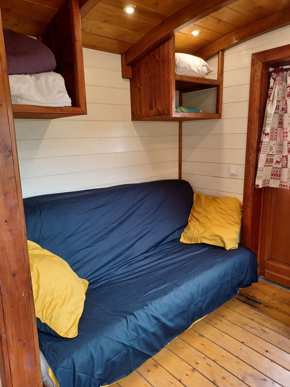 A wooden cabin interior with a blue sofa, yellow pillows, and wooden shelves above. - Roulottes a la Ferme sur le Plateau du Vercors (Autrans-Méaudre en Vercors)