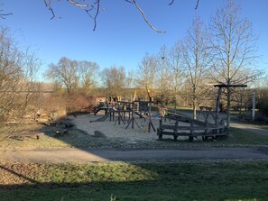 Ein Spielplatz mit Klettergerüsten und einer Rutsche, umgeben von Bäumen und einem Feldweg.