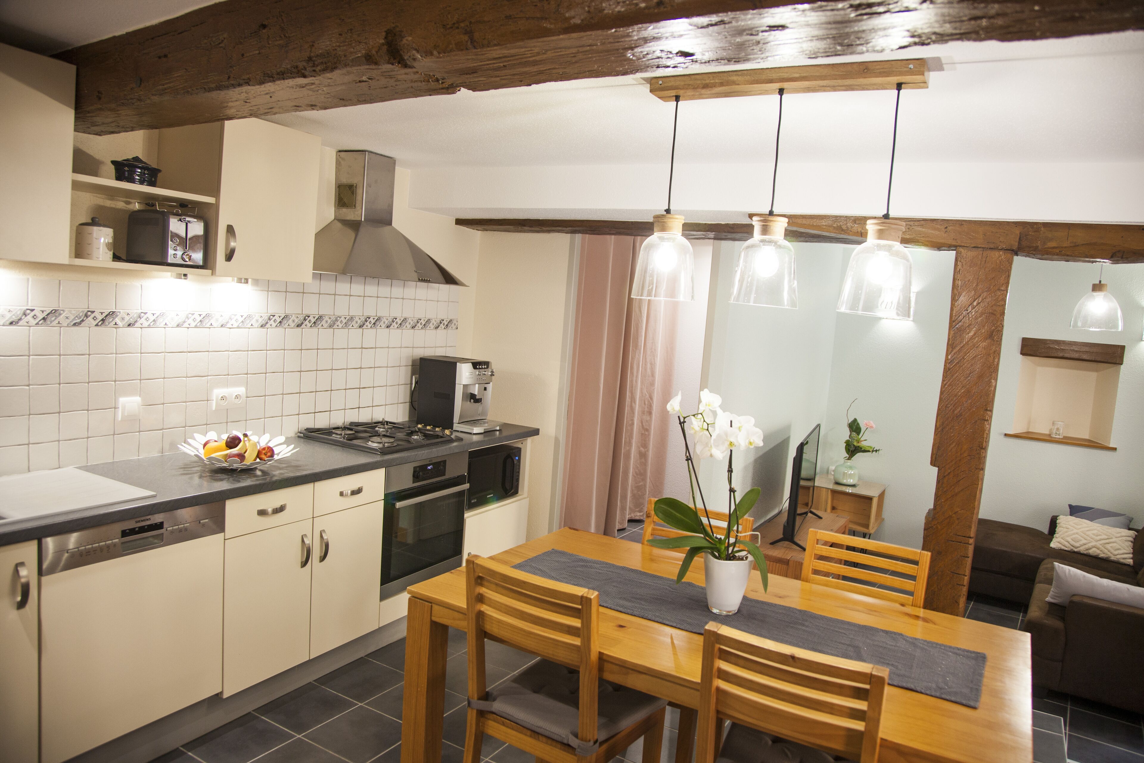 A modern kitchen with a dining area, featuring a wooden table, chairs, and pendant lights.