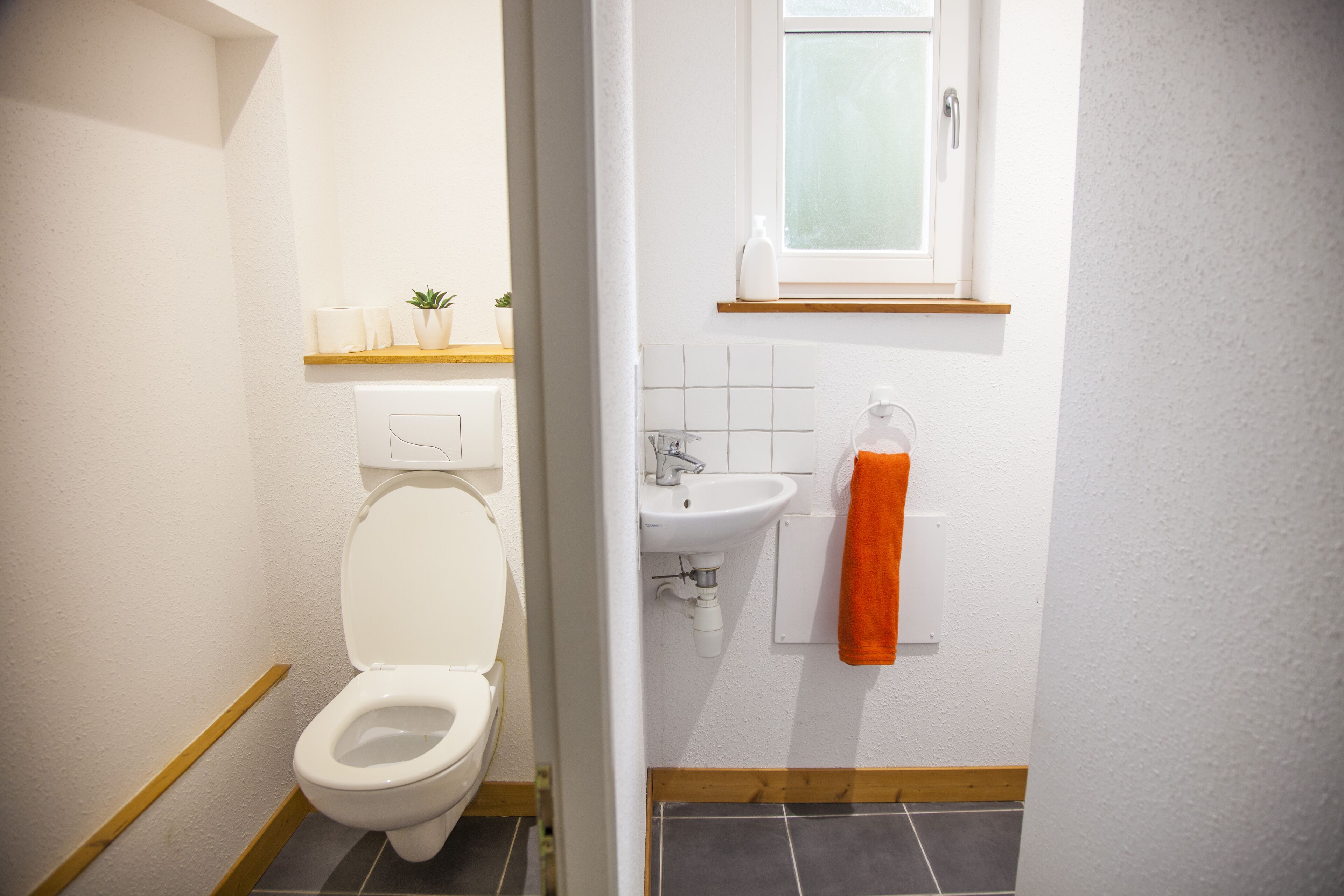 Un baño con inodoro, lavamanos y una ventana sobre el lavamanos.