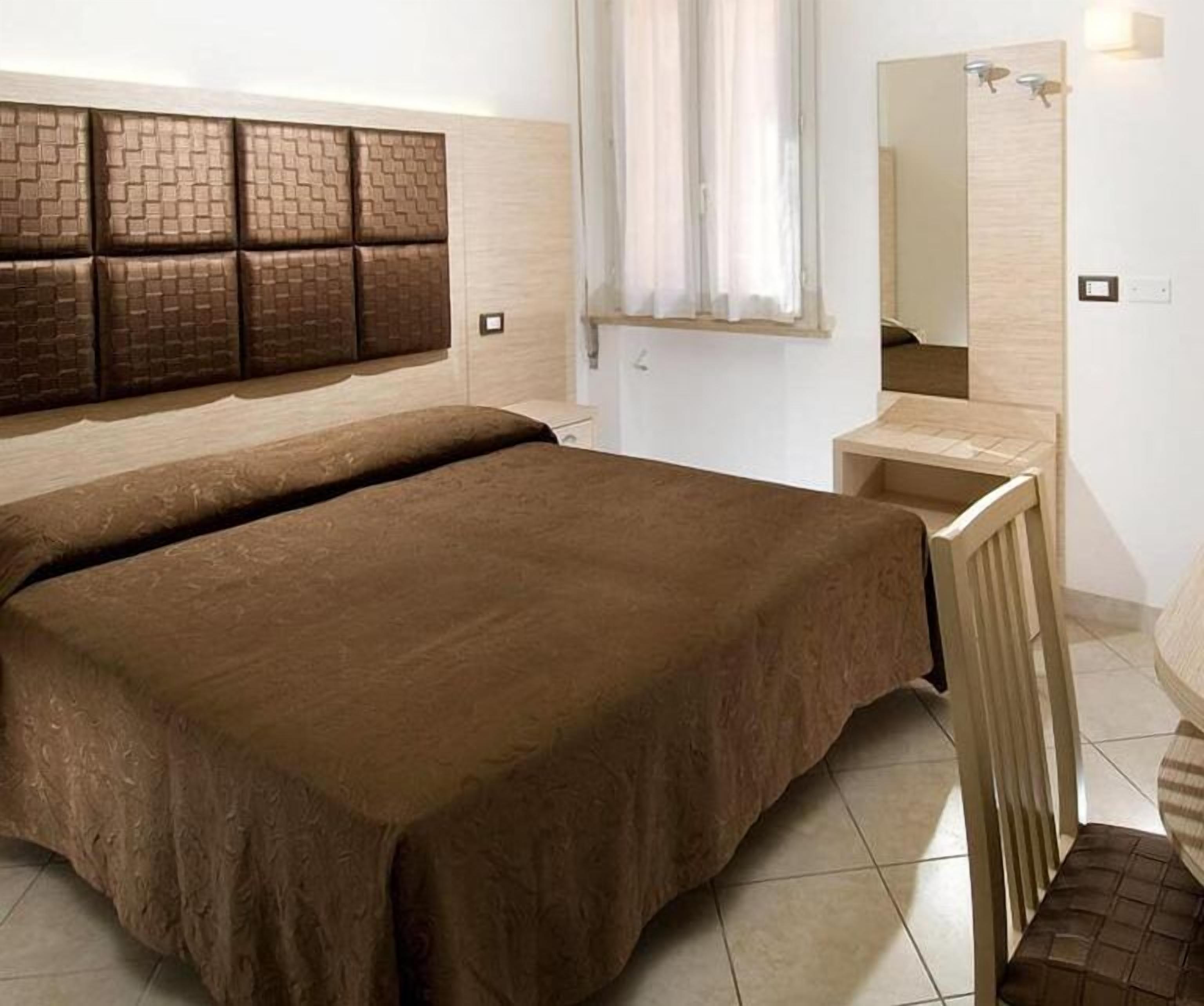 A bedroom with a large bed, a bedside table, a mirror, and a window with curtains.