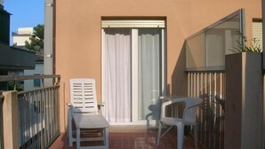A balcony with two white plastic chairs, a small table, and a sliding glass door. - Hotel D'annunzio (Cattolica)