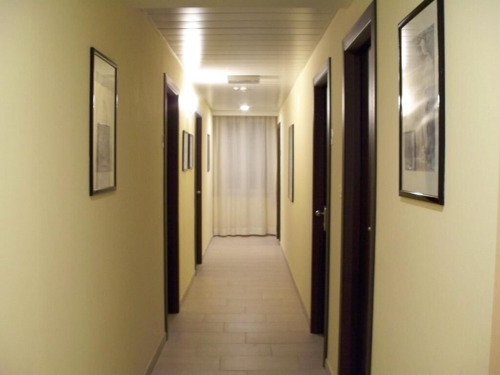Un pasillo con puertas a ambos lados, cuadros en las paredes y una fuente de luz al final.