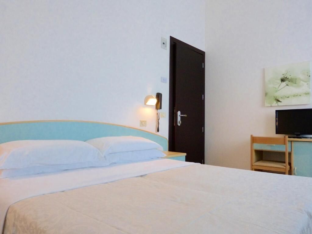 A hotel room with a bed, a nightstand with a lamp, a television, and a door.