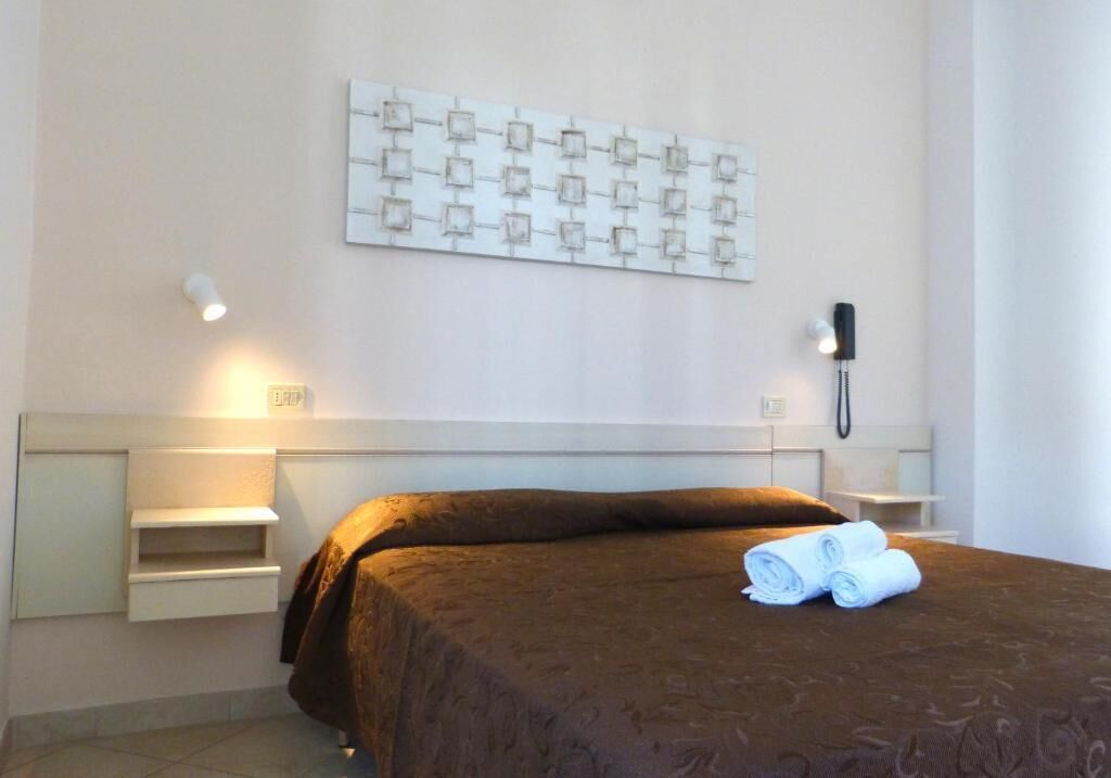Una habitación de hotel con cama, teléfono en la pared y una lámpara.