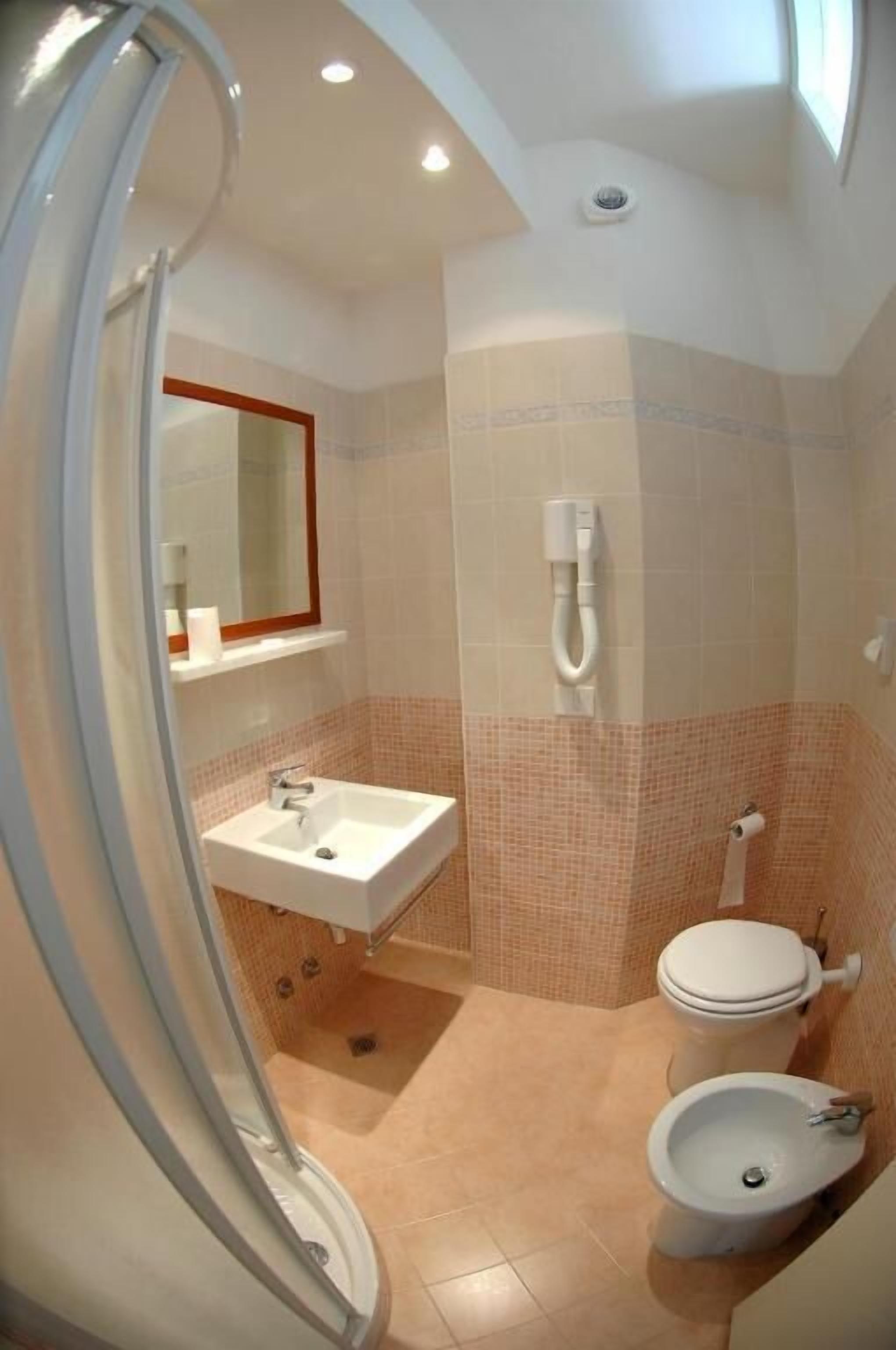 Un baño con lavamanos, inodoro y bidé, con paredes de azulejos y un espejo.