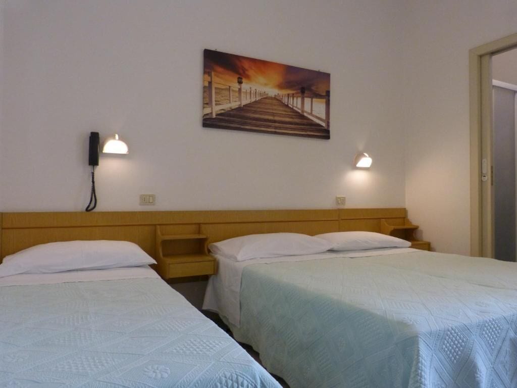 A hotel room with two single beds, a wooden headboard, a painting of a pier, and bedside lamps.
