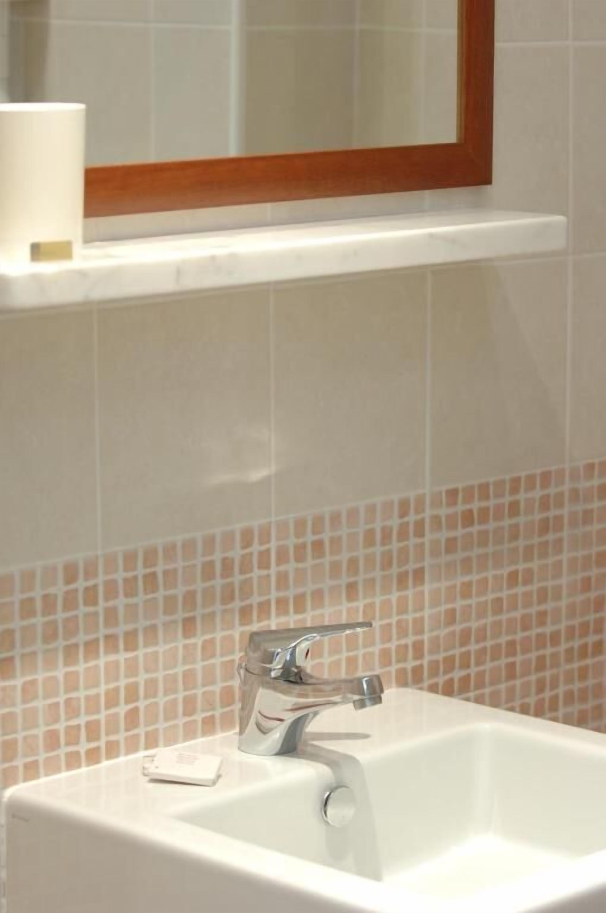 A bathroom with a white sink, a mirror with a wooden frame, and a tiled backsplash.
