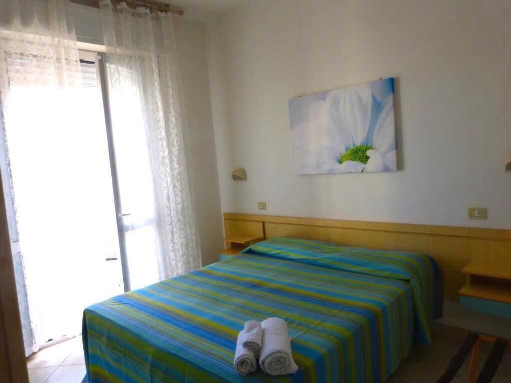 Une chambre d’hôtel avec un lit, un tableau au mur et une fenêtre avec des rideaux.