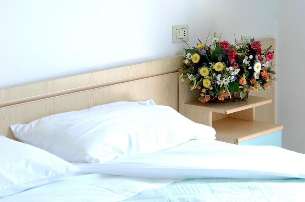 A neatly made bed with white linens, a wooden headboard, and a bedside table with a floral arrangement.