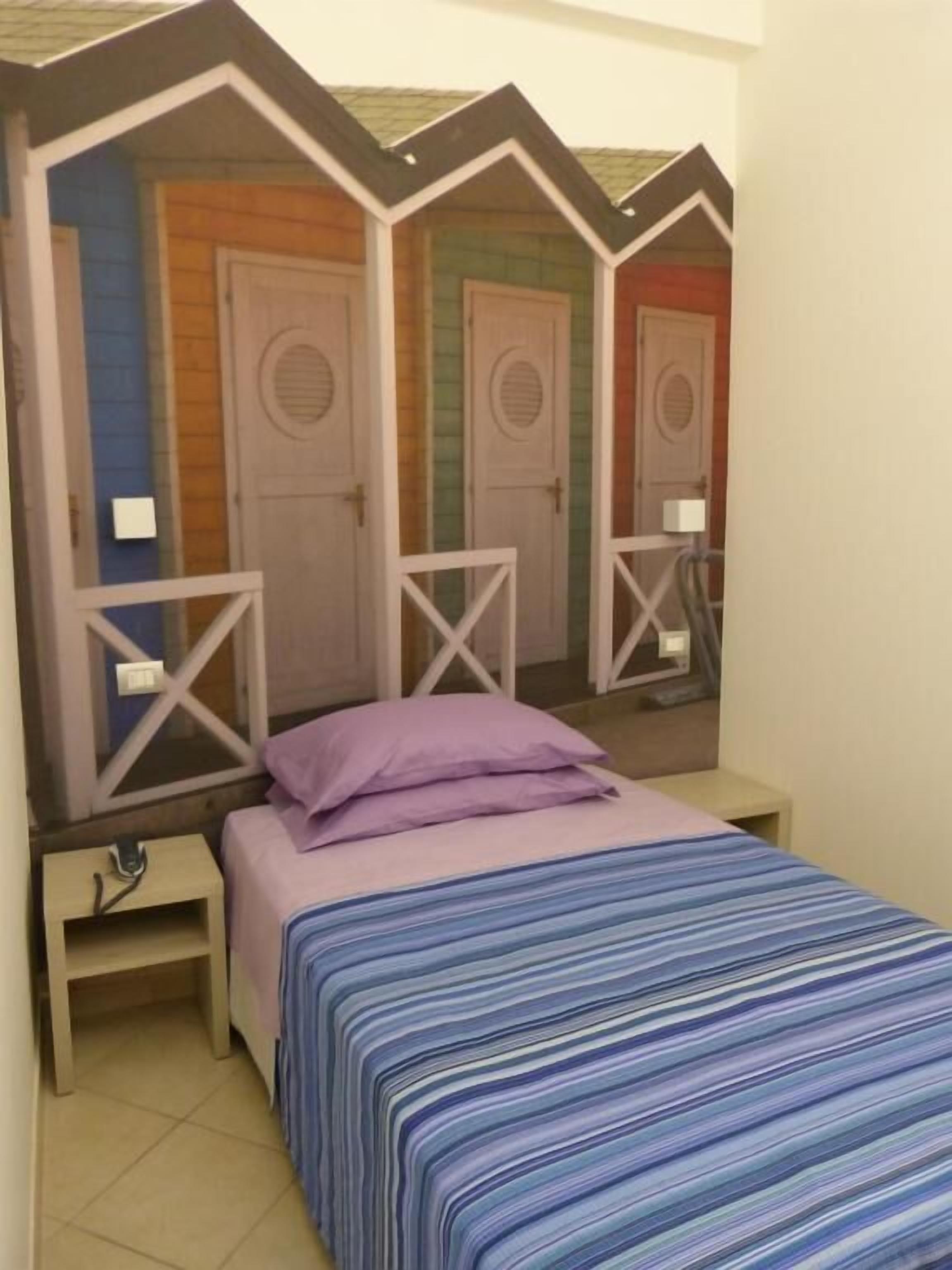 Una habitación con una cama, una mesita de noche y un espejo. Se ven tres puertas al fondo.