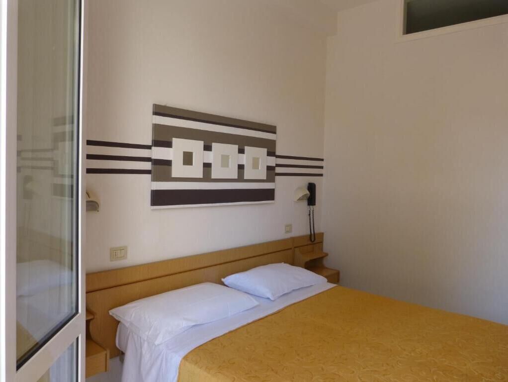A bedroom with a bed, a wall-mounted telephone, and a window.