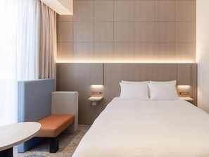 Une chambre d’hôtel moderne avec un grand lit, des tables de chevet, un banc et une petite table.
