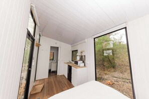 Ein modernes Interieur mit Küchenbereich, Essbereich und einem großen Fenster mit Blick ins Freie.