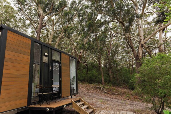 A modern cabin with a wooden exterior, large windows, and a deck with outdoor seating.