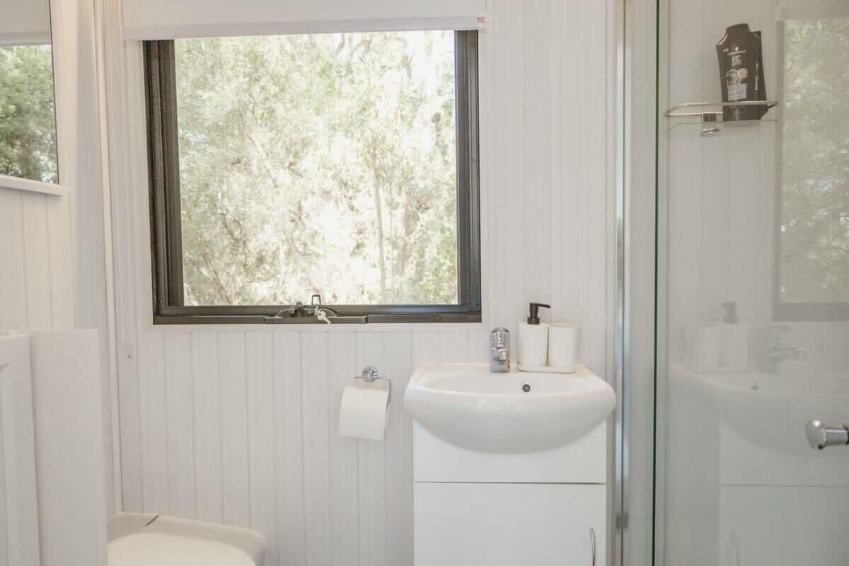 A bathroom with a window, a sink, a toilet, and a shower area.