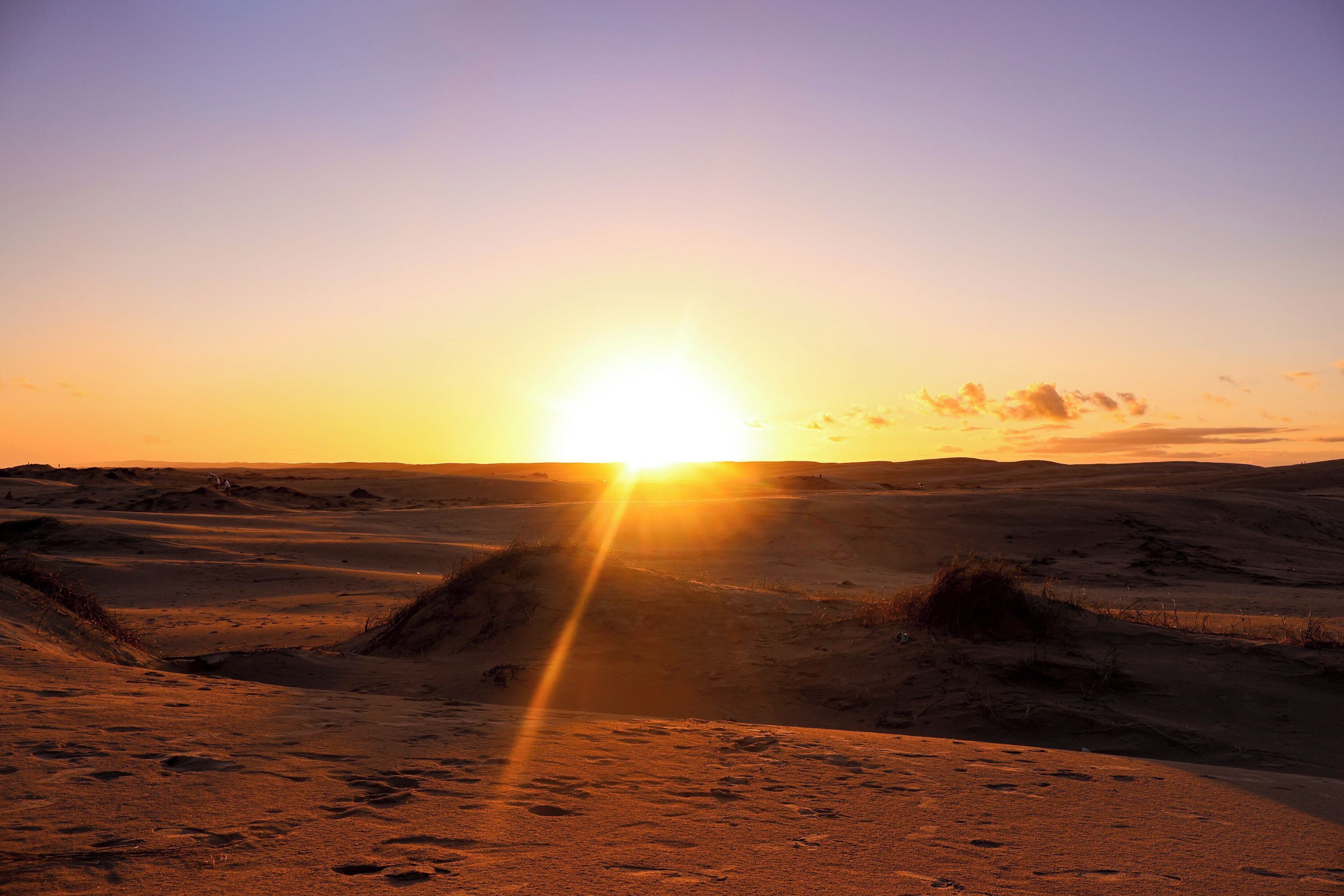A desert landscape with dunes and a sunset.