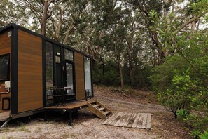 Une petite cabane en bois dotée d’une terrasse et d’un escalier menant à l’entrée.