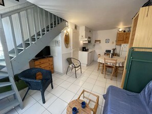 A compact living space with a staircase, a dining area, a kitchen, and a seating area with a sofa and chairs. - Cozy 3-Room House with Access to Pools and Close to Beach, Sleeps 4 (Saint-Jean-de-Monts)