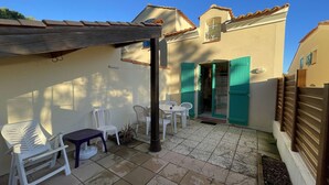 A patio area with a pergola, white plastic chairs, a small table, and a tiled floor.