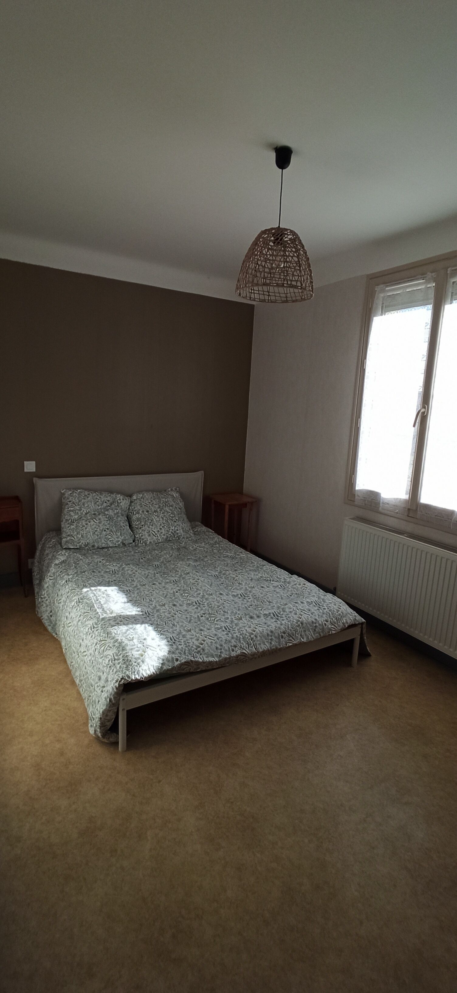 Ein Schlafzimmer mit Bett, einer Pendelleuchte, einem Fenster und einer Heizung.