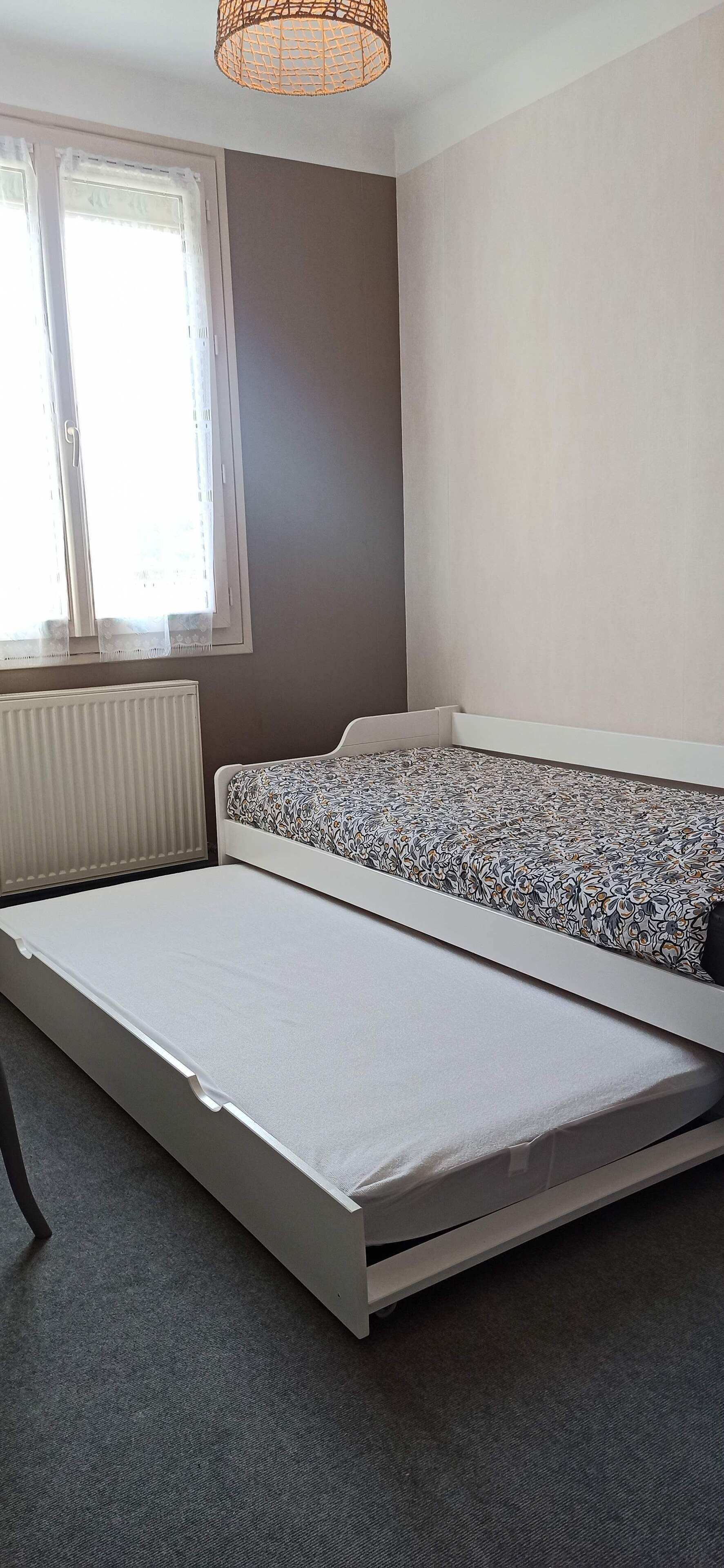 Ein Schlafzimmer mit einem Bett, einem Fenster mit Vorhängen, einem Heizkörper und einer Pendelleuchte.