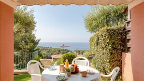 Une terrasse avec une table dressée pour le petit-déjeuner, offrant une vue panoramique sur la mer et la verdure.