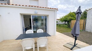 A patio with a table and chairs, a covered umbrella, and a view of a garden and fence. - New Downtown House w/ Garden, Parking, WIFI & A/C - 500m to Beach (La Tranche-sur-Mer)
