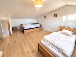Une chambre avec un plancher en bois, un lit avec une literie blanche, une table de chevet et une lampe sur pied.