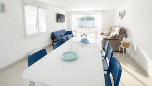 A bright, modern living room with a white dining table, blue chairs, and a beige sofa. - New Downtown House w/ Garden, Parking, WIFI & A/C - 500m to Beach (La Tranche-sur-Mer)